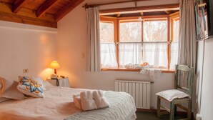 A cozy bedroom with a bed, a chair, a table with a lamp, and a window with curtains. - Hosteria El Arbol Duende (San Martín de los Andes)