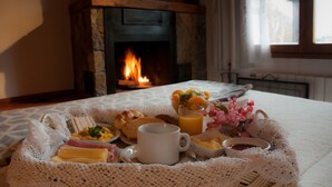 A breakfast tray with croissants, eggs, butter, and juice on a table with a fireplace in the background. - Hosteria El Arbol Duende (San Martín de los Andes)