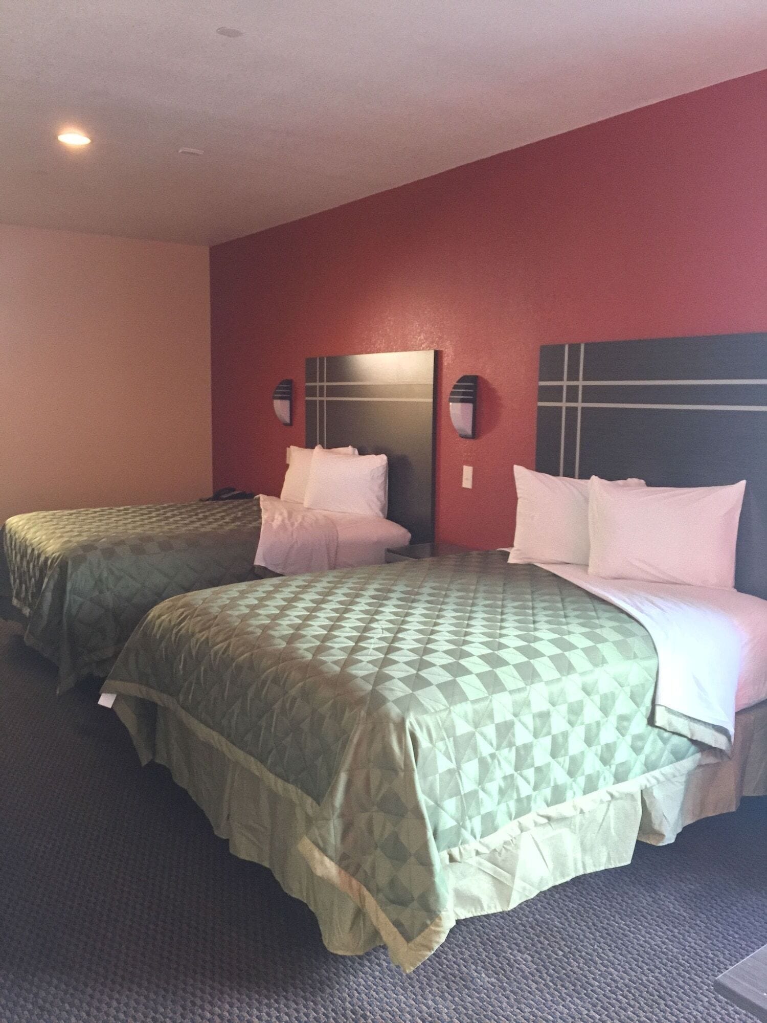 A hotel room with two beds, each with a headboard and pillows, and a red accent wall.