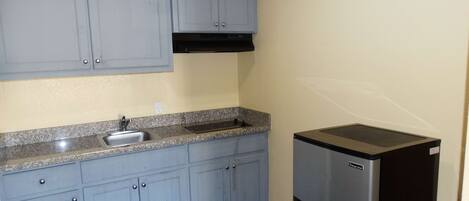 A small kitchen with light blue cabinets, a stainless steel sink, and a black refrigerator.
