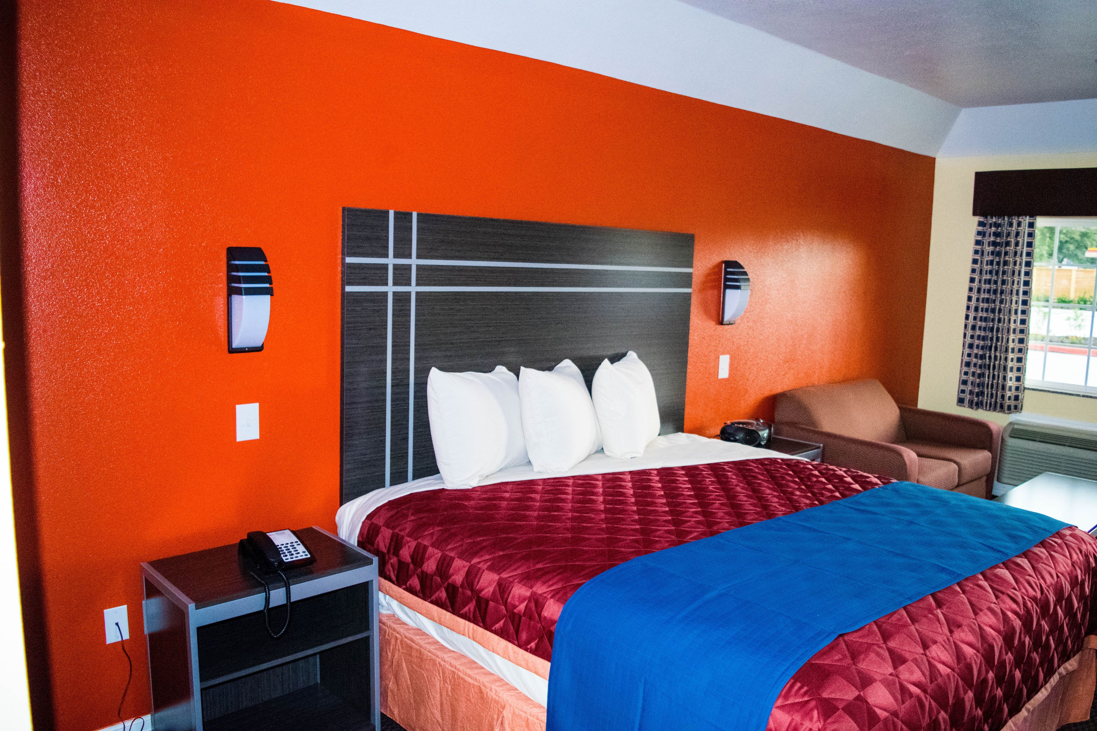 A hotel room with a large bed, a desk with a telephone, a chair, and a window with curtains.