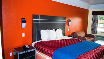 A hotel room with a large bed, a desk with a telephone, a chair, and a window with curtains.