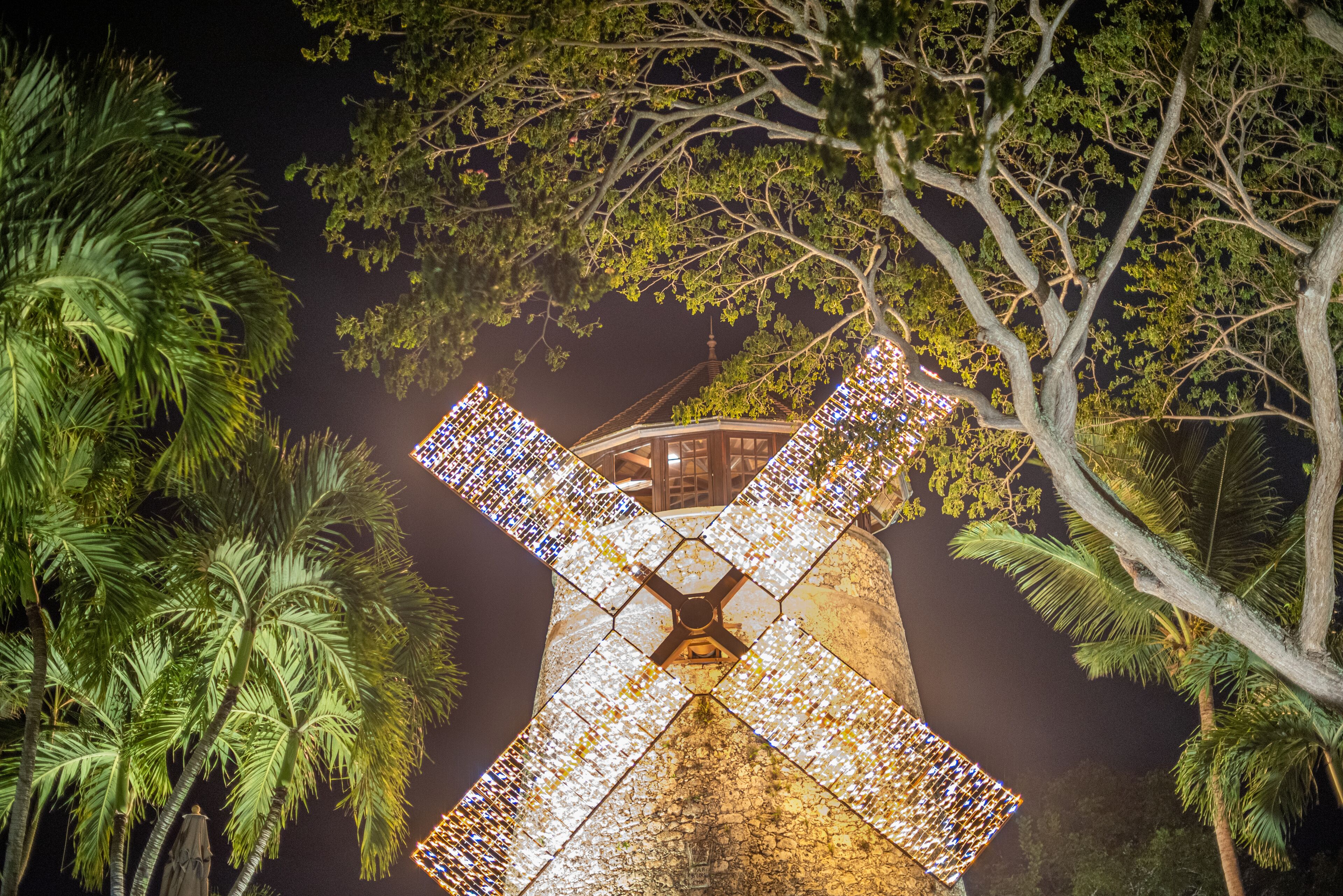 Un molino de viento con una gran estructura en forma de X iluminada, rodeado de árboles.