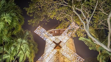 A windmill with a large, illuminated X-shaped structure, surrounded by trees.