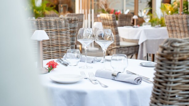 A dining table set with white tablecloth, wicker chairs, and clear glassware. - Le Relais du Moulin, Hôtel de Charme & Spa (Sainte-Anne)