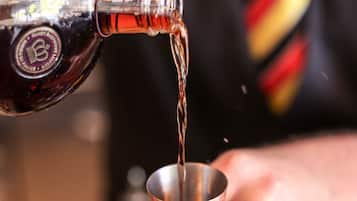 Una persona vertiendo un líquido oscuro de una botella en una taza de metal.