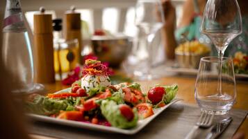 Una mesa de comedor con ensalada, copas de vino y cubiertos.