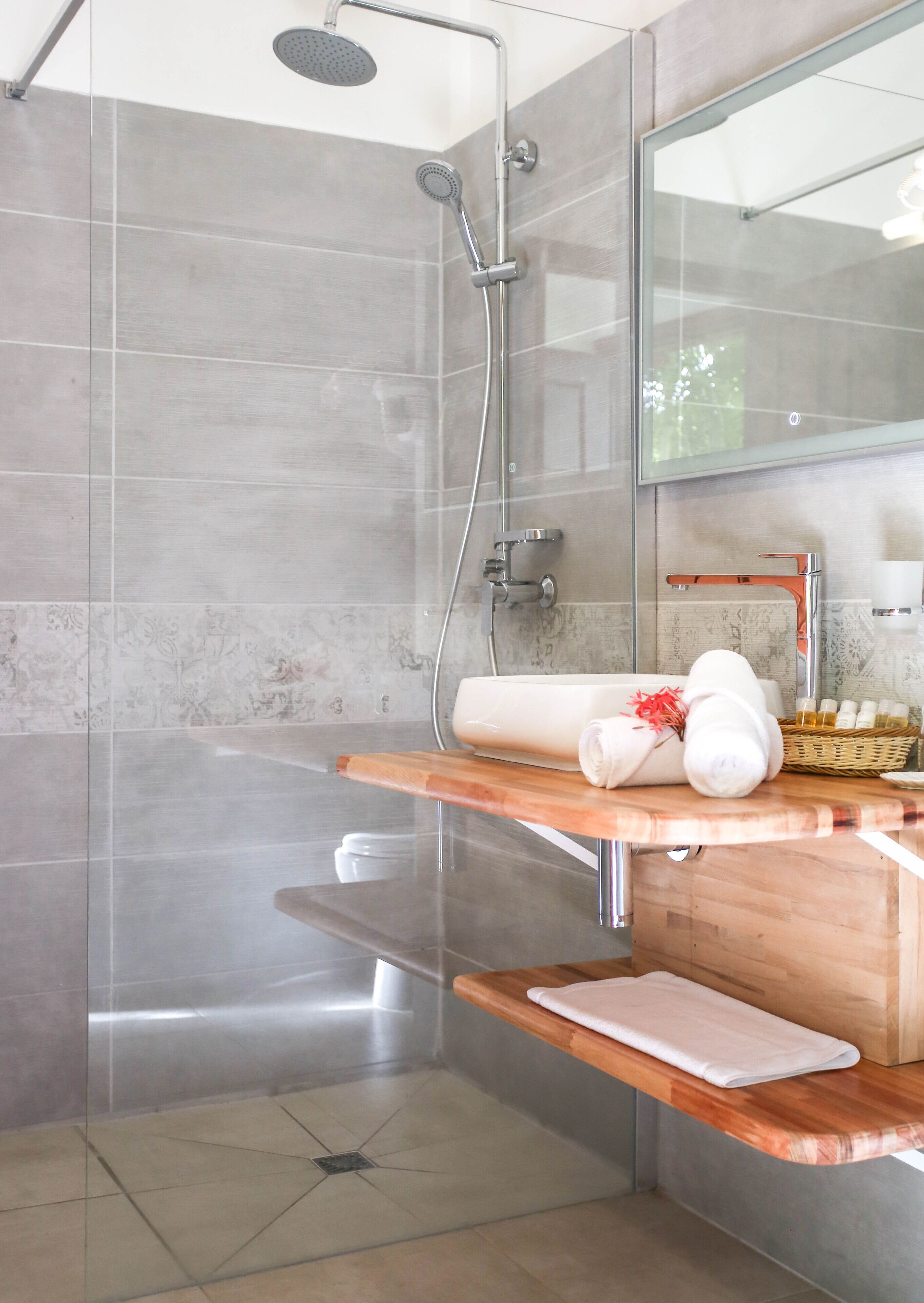 A modern bathroom with a glass shower enclosure, a wooden vanity with a towel rack, and a mirror.