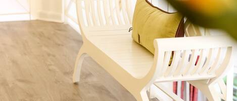 A white bench with a yellow cushion in a room with wooden flooring and white walls.