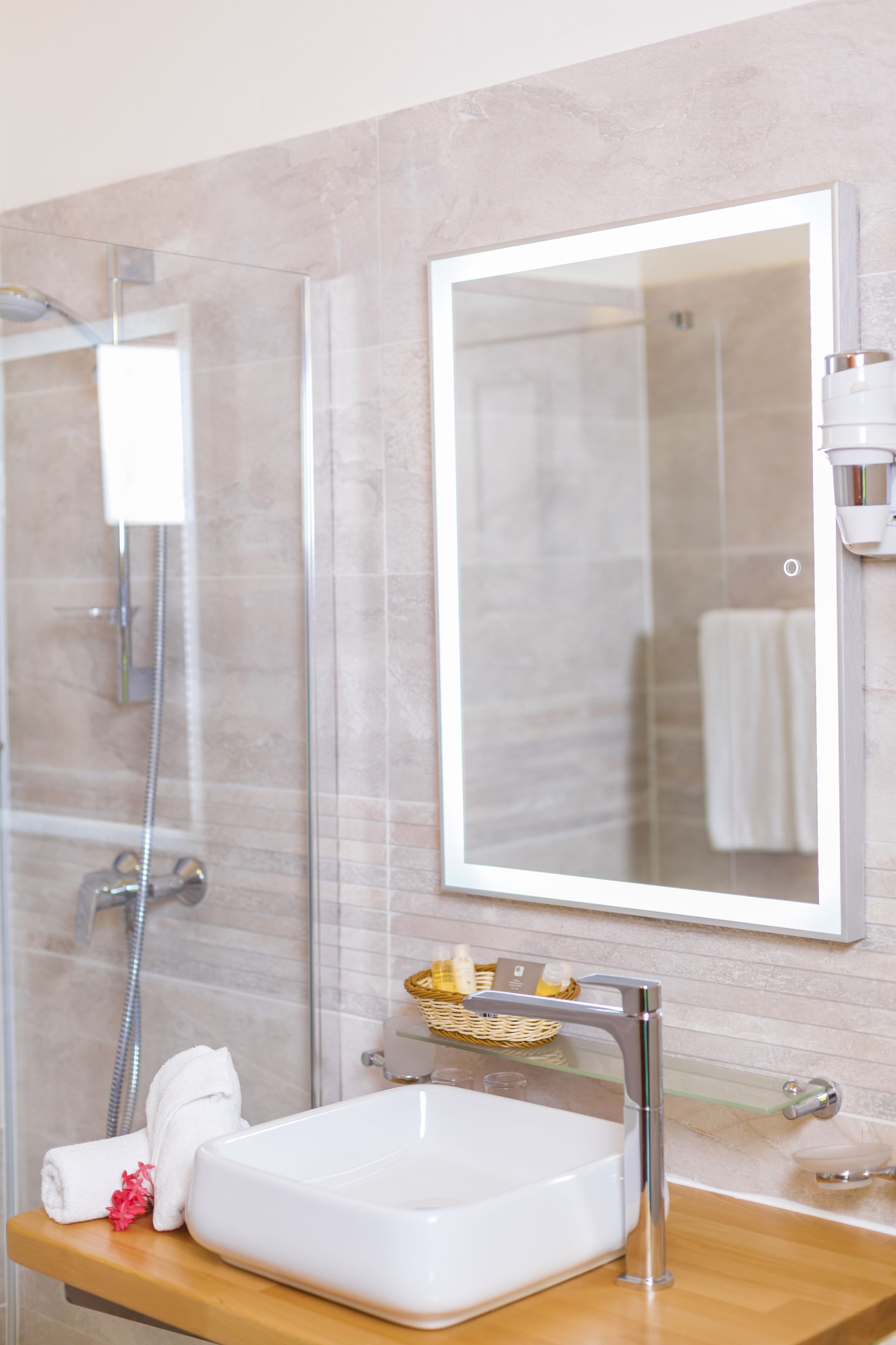 A bathroom with a glass shower enclosure, a white sink, a mirror, and a wooden countertop.