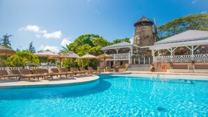 A pool area with lounge chairs and umbrellas, a stone tower, and a building with a thatched roof. - Le Relais du Moulin, Hôtel de Charme & Spa (Sainte-Anne)