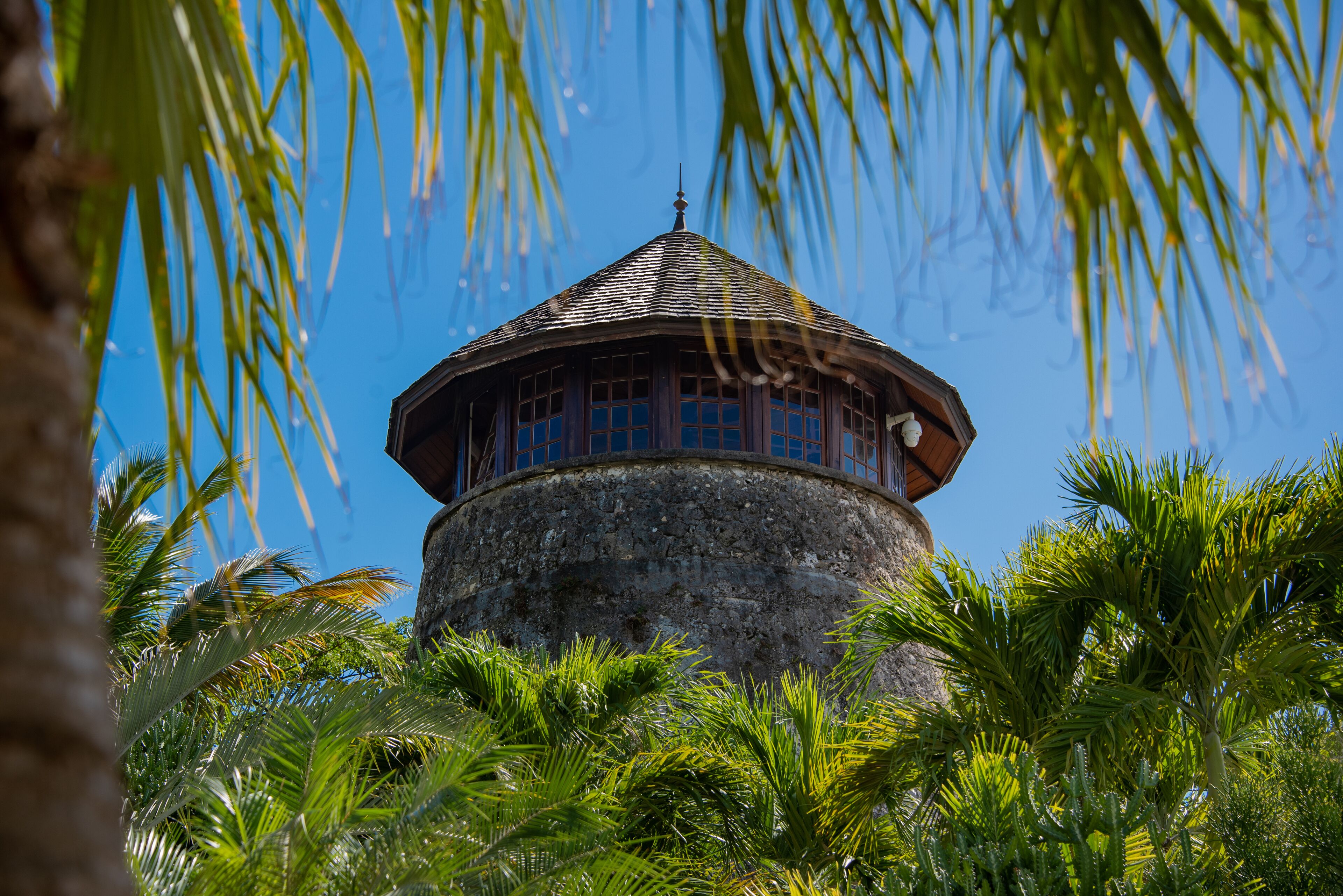 Una torre redonda con techo cónico, rodeada de exuberante vegetación y palmeras.