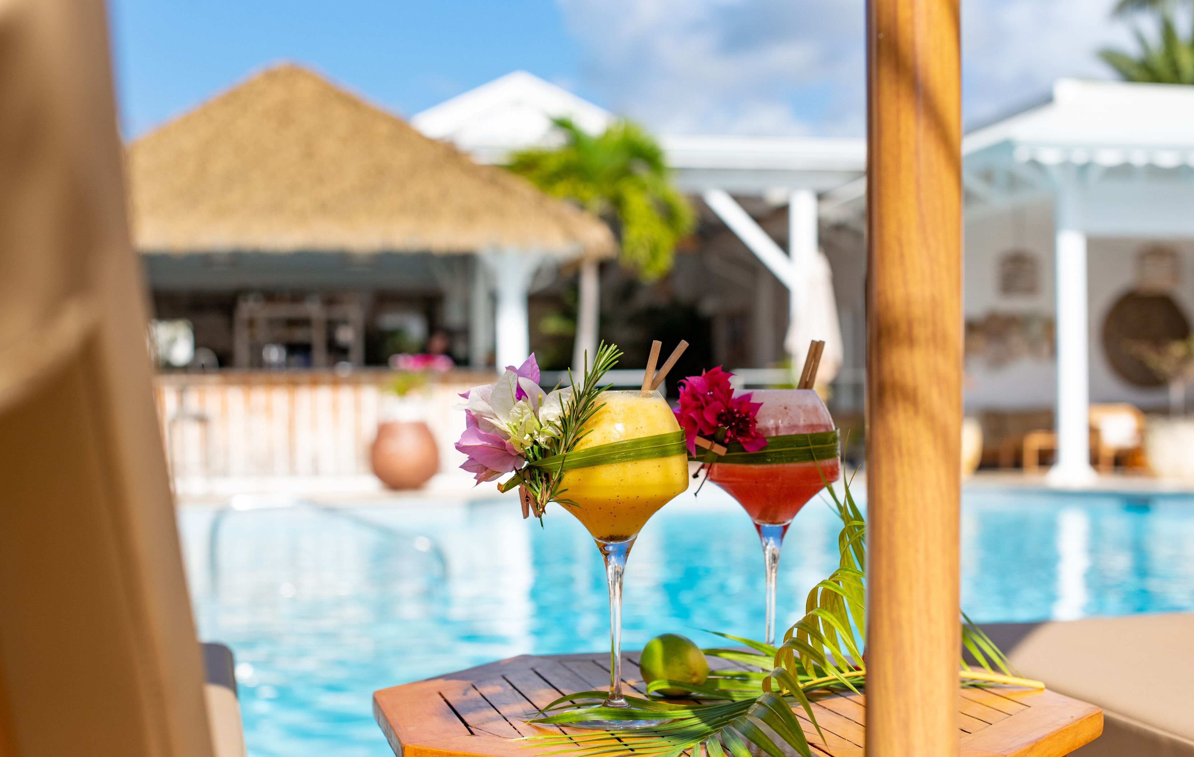 A poolside view with two cocktails garnished with flowers and a tropical setting.