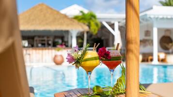 A poolside view with two cocktails garnished with flowers and a tropical setting.