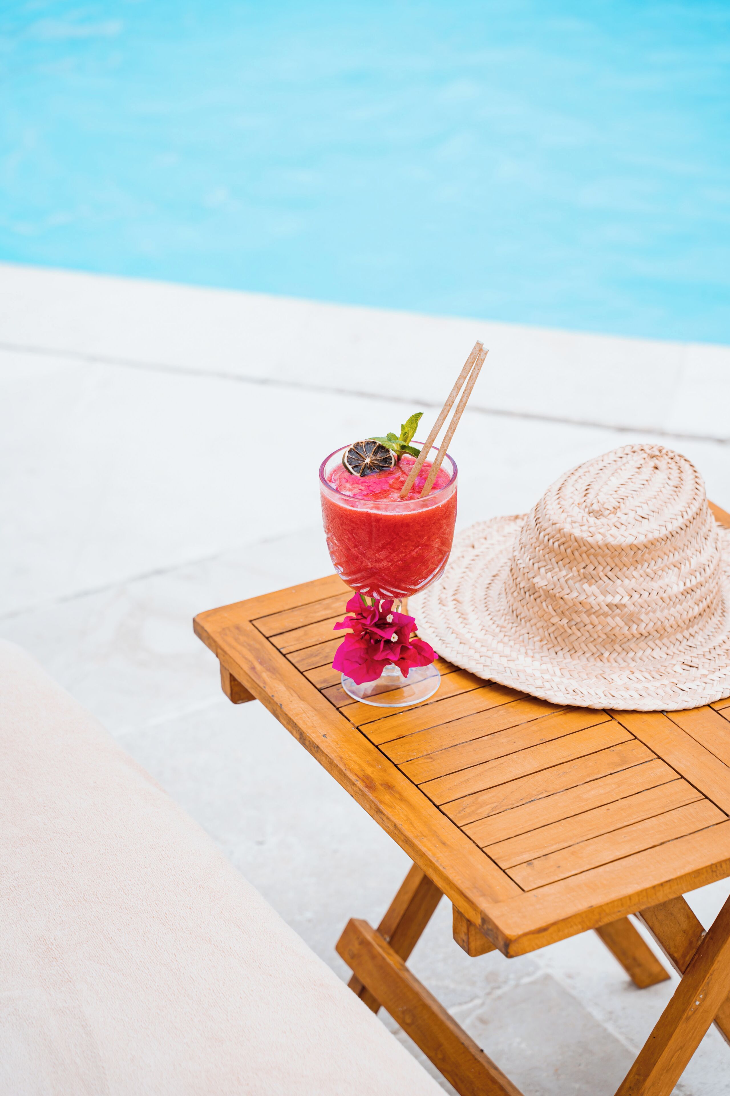 A wooden table with a drink and a straw hat.