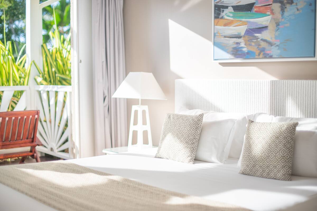 A bedroom with a large bed, white bedding, a white lamp, and a painting on the wall.