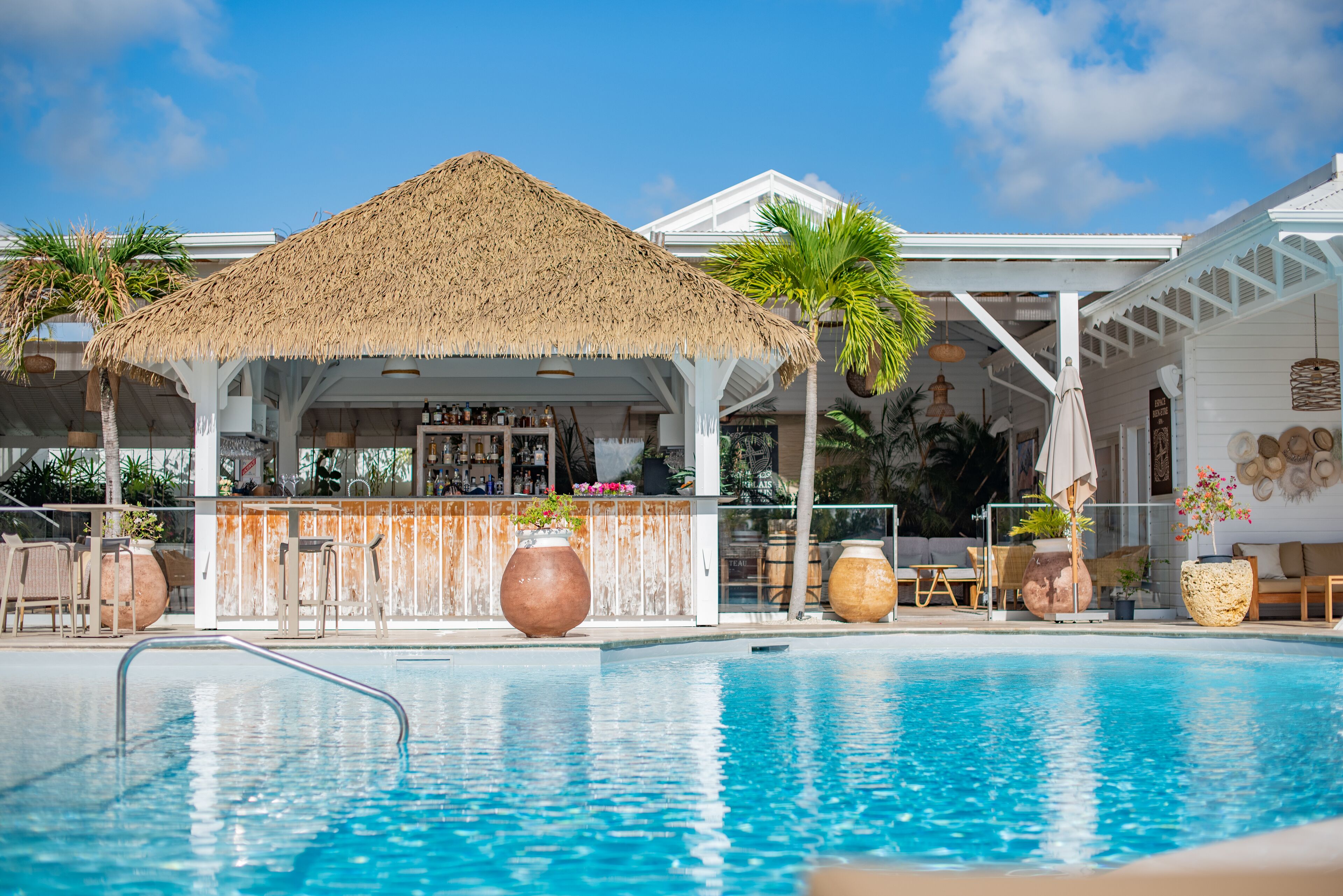 A poolside bar with a thatched roof, surrounded by lounge chairs and potted plants.