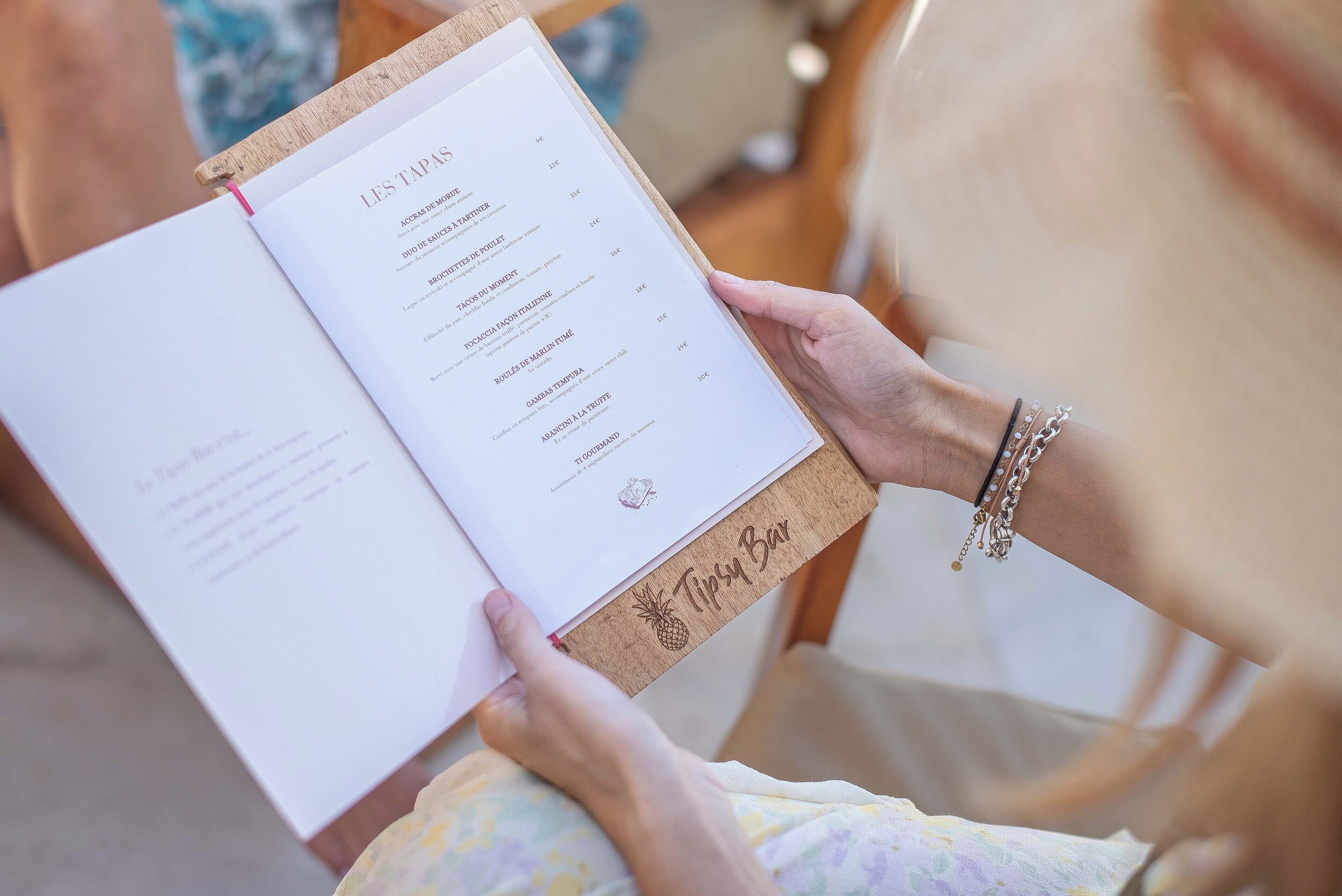 A person holding a menu with the title "LES TAPAS" and various food items listed.