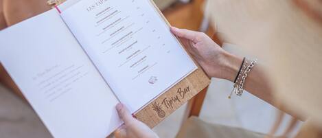 A person holding a menu with the title "LES TAPAS" and various food items listed.