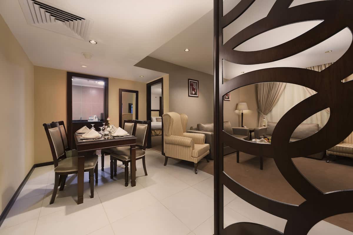 A hotel room with a dining area, a sofa, a chair, and a decorative partition.
