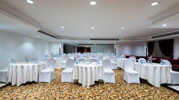 Une salle de banquet avec des tables rondes, des chaises blanches et un tapis à motifs.