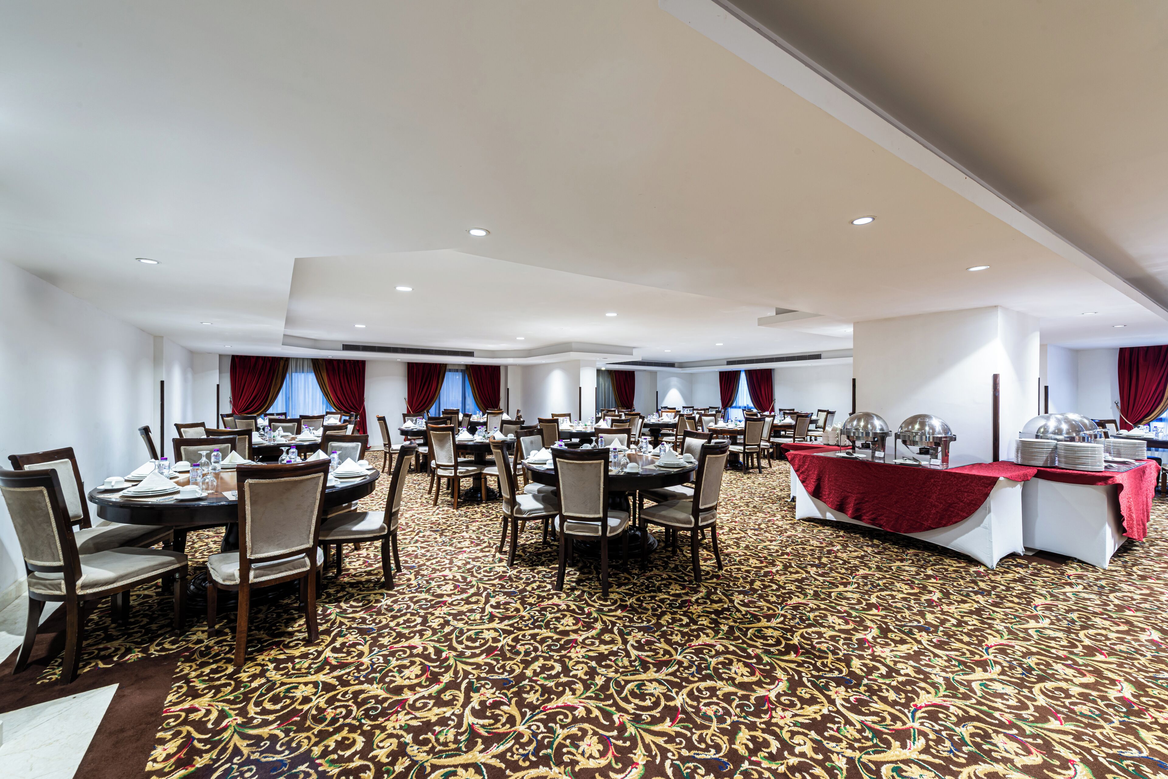 Een ruime balzaal met meerdere ronde tafels, stoelen en een buffet.