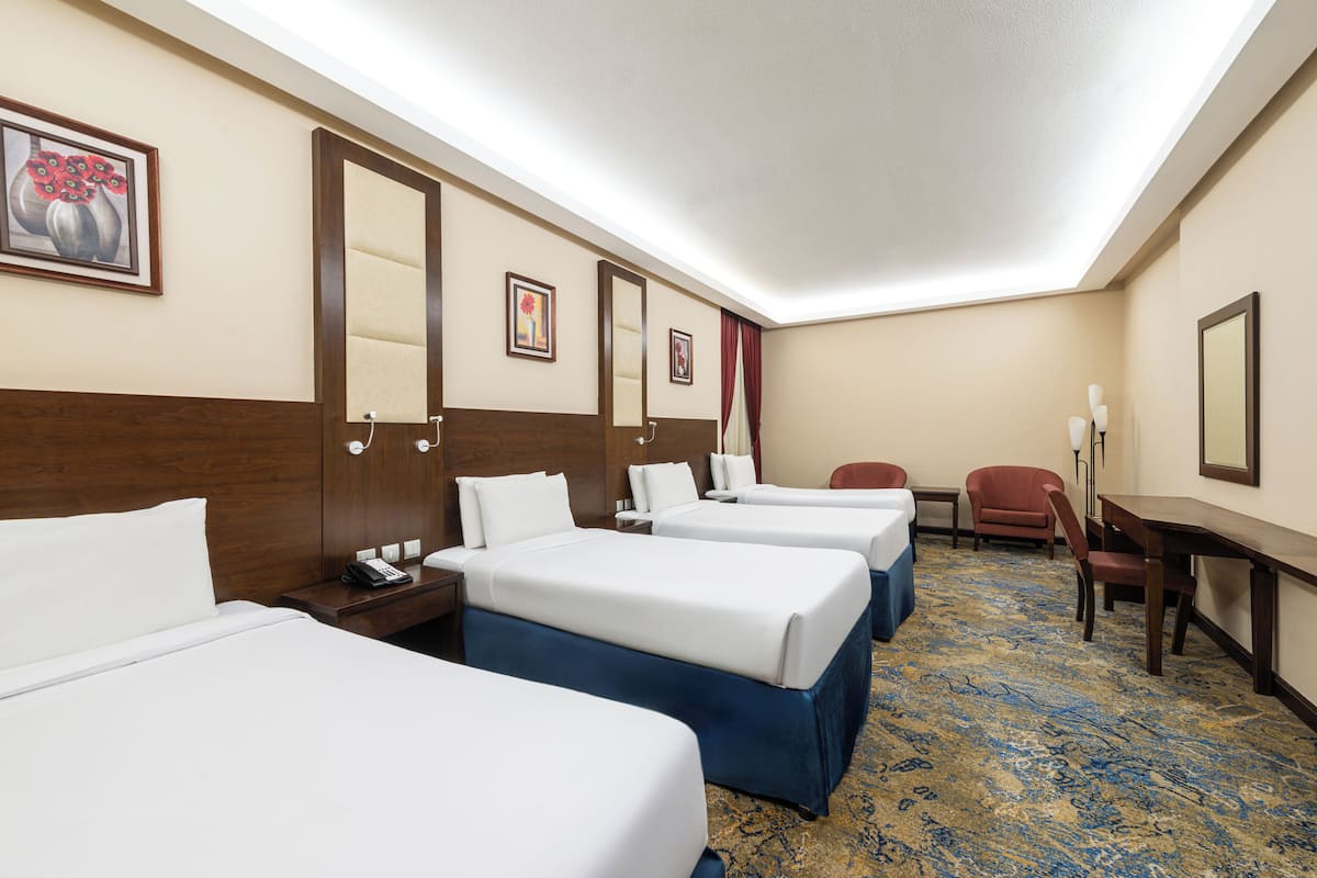 A hotel room with three beds, a desk, a chair, and a carpeted floor.