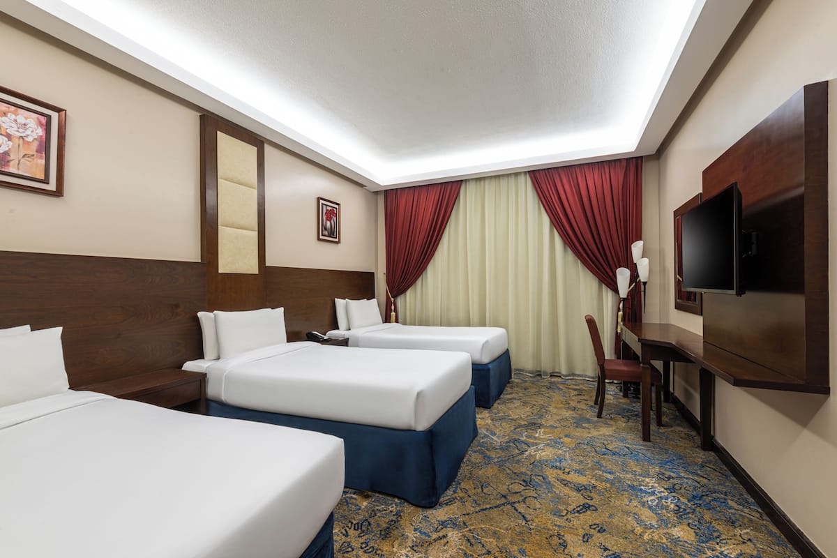 A hotel room with three beds, a television, a desk, and a chair.