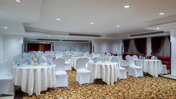 A banquet hall with round tables, white chairs, and a patterned carpet.
