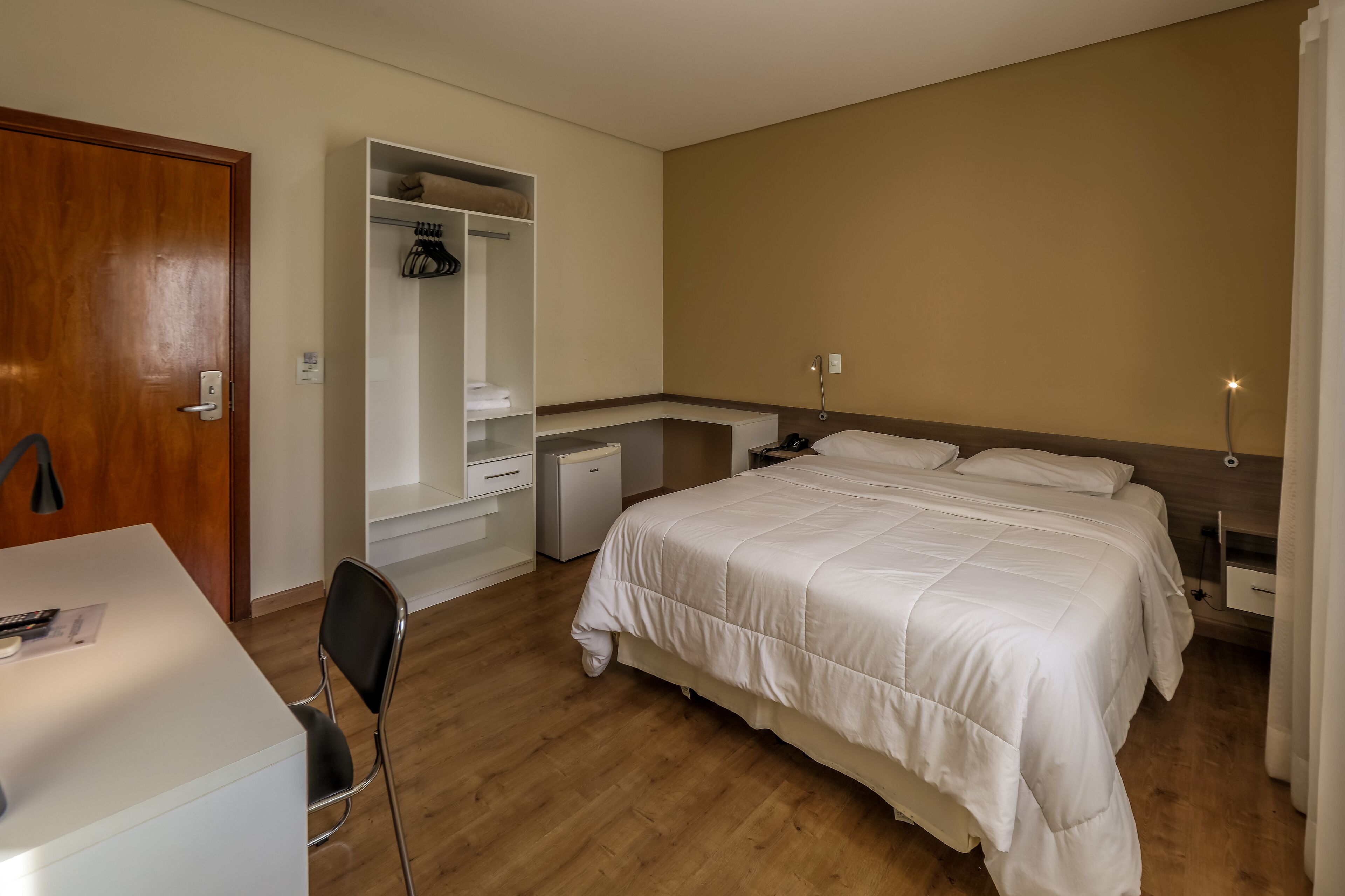 A bedroom with a bed, bedside tables, a desk, a chair, a wardrobe, and a small desk lamp.