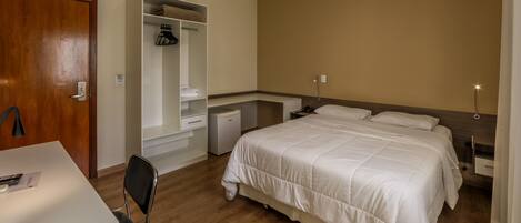 A bedroom with a bed, bedside tables, a desk, a chair, a wardrobe, and a small desk lamp.