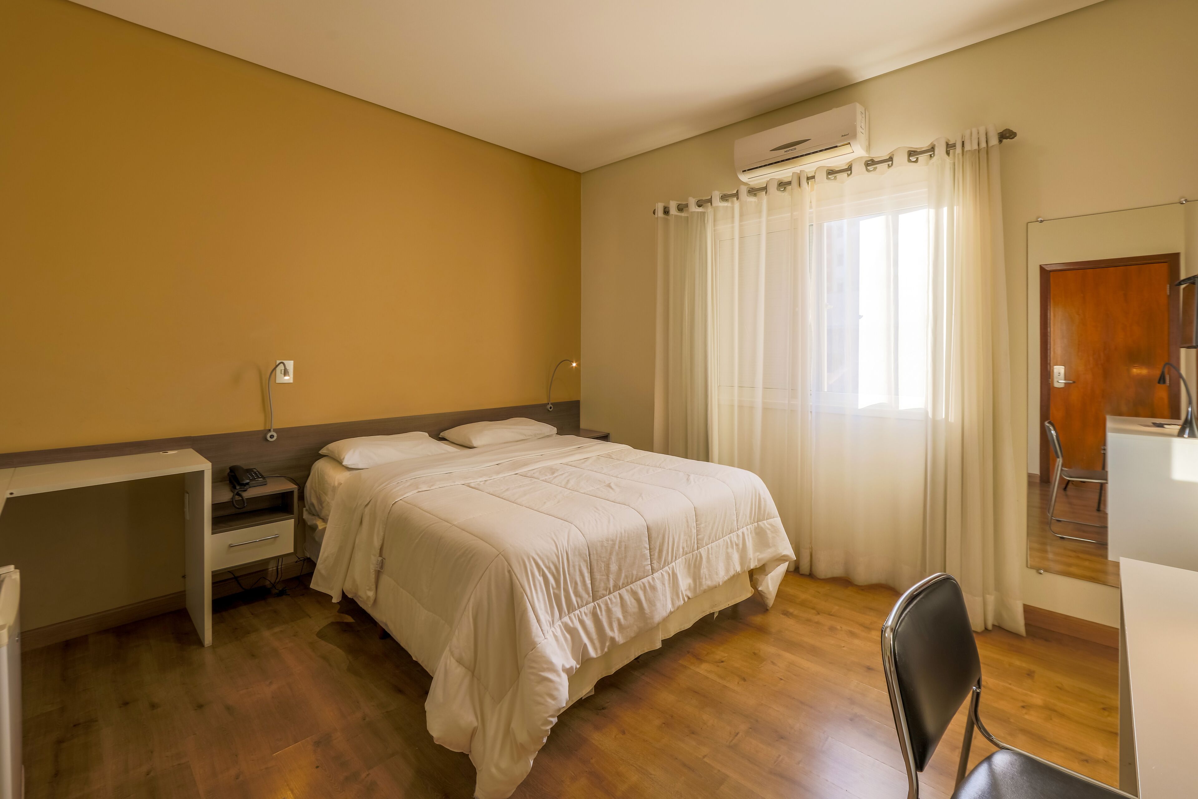 A bedroom with a bed, a desk, a chair, and a window with curtains.