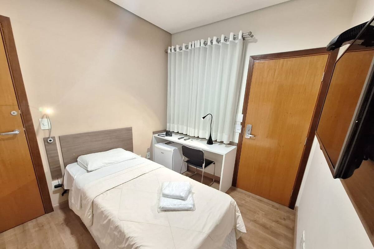 A hotel room with a bed, a desk, a chair, and a wardrobe.