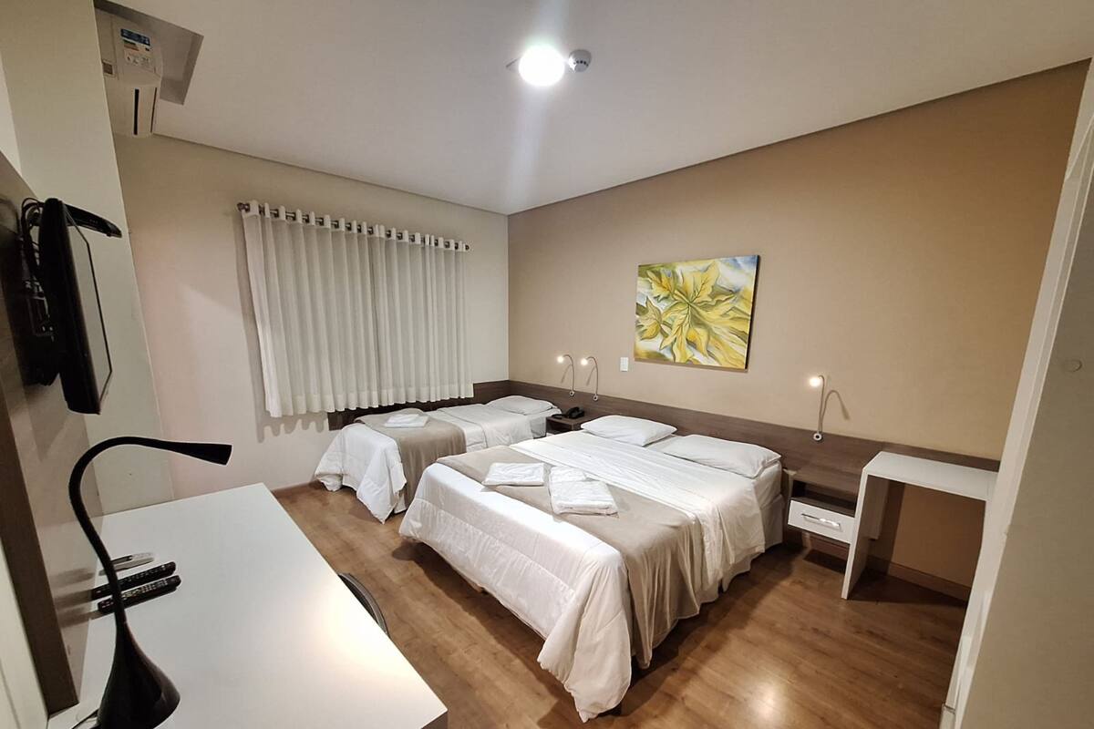 A hotel room with two beds, a desk, a chair, a nightstand, a painting, and a window with curtains.
