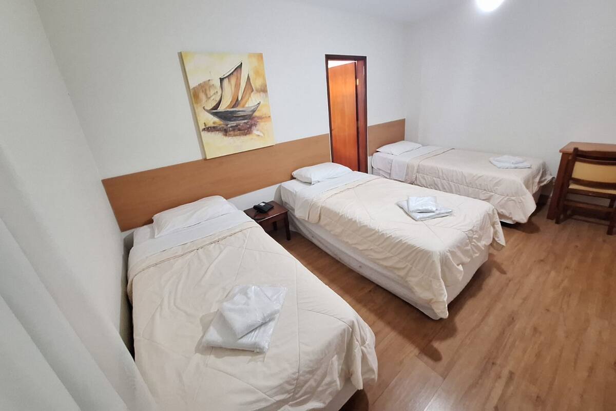 A hotel room with three single beds, a wooden desk, and a painting on the wall.