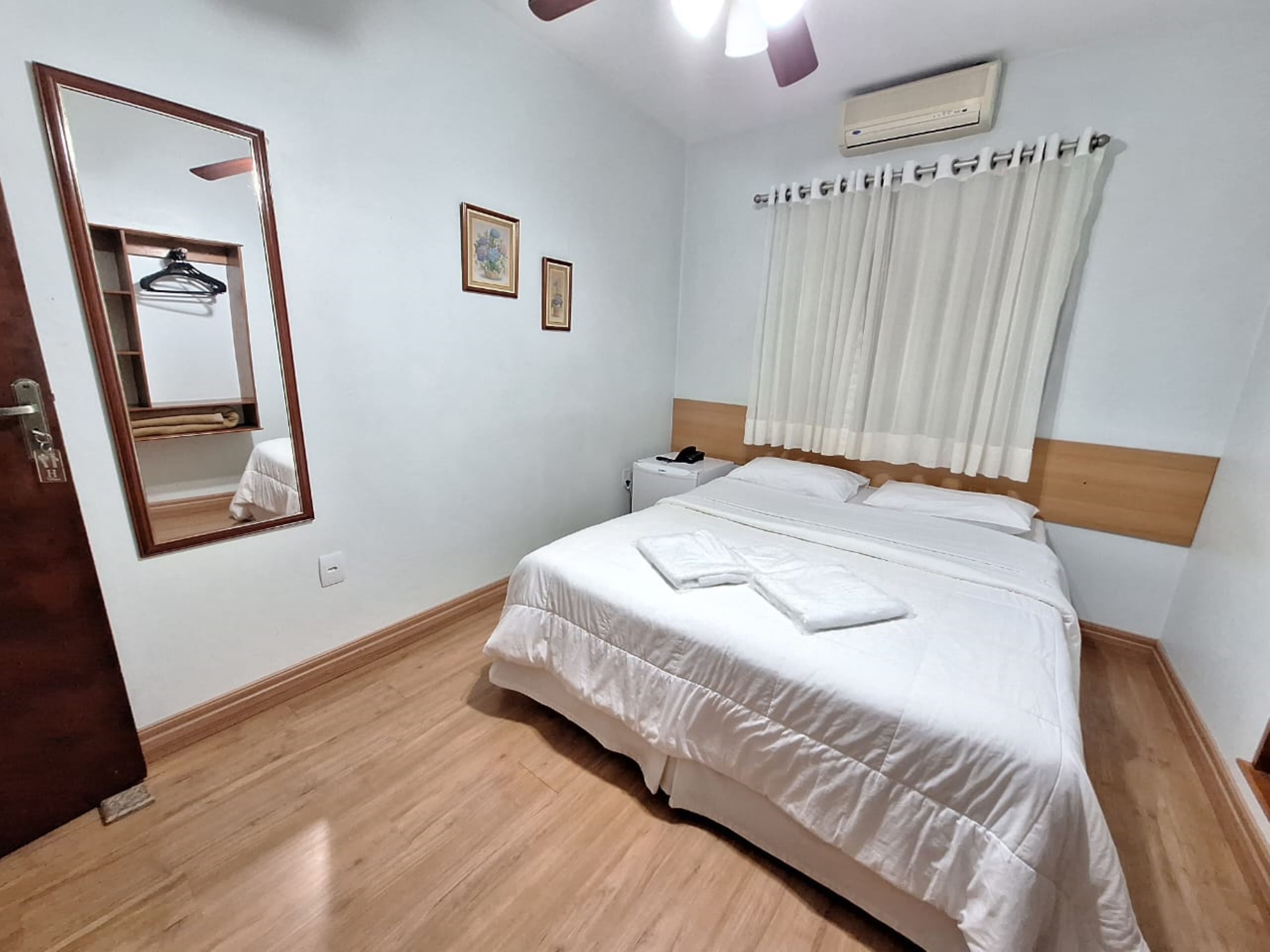 Une chambre d’hôtel avec un lit, une table de chevet, un miroir et une fenêtre avec des rideaux.