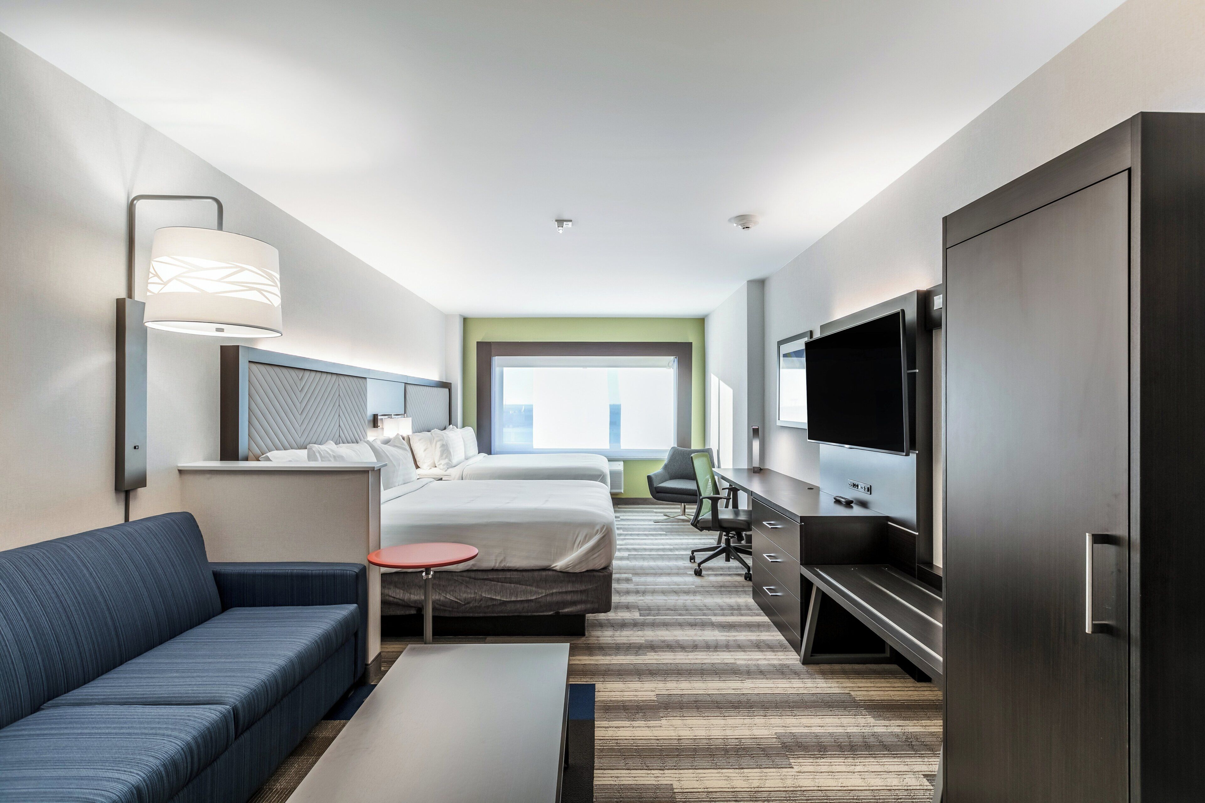 A hotel room with a bed, a sofa, a TV, a desk, and a window.