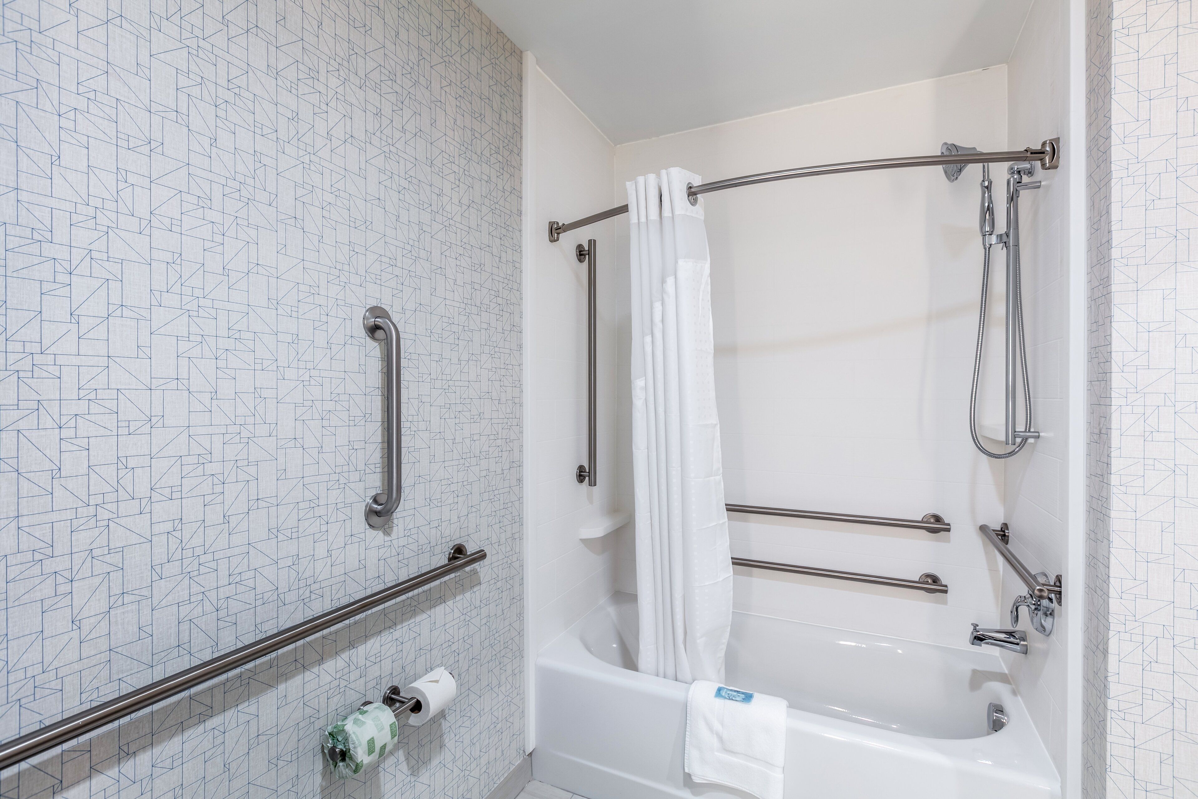 Ein Badezimmer mit einer weißen Badewanne, einer Dusche mit Glastür und einer Wand mit Muster.