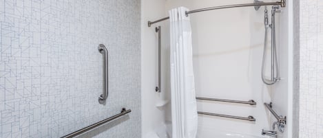 Un baño con una bañera blanca, ducha con puerta de vidrio y pared con diseño.
