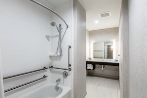 A modern bathroom with a bathtub, shower, and handrails.