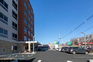 A parking lot with cars, a building with multiple floors, and a clear blue sky.