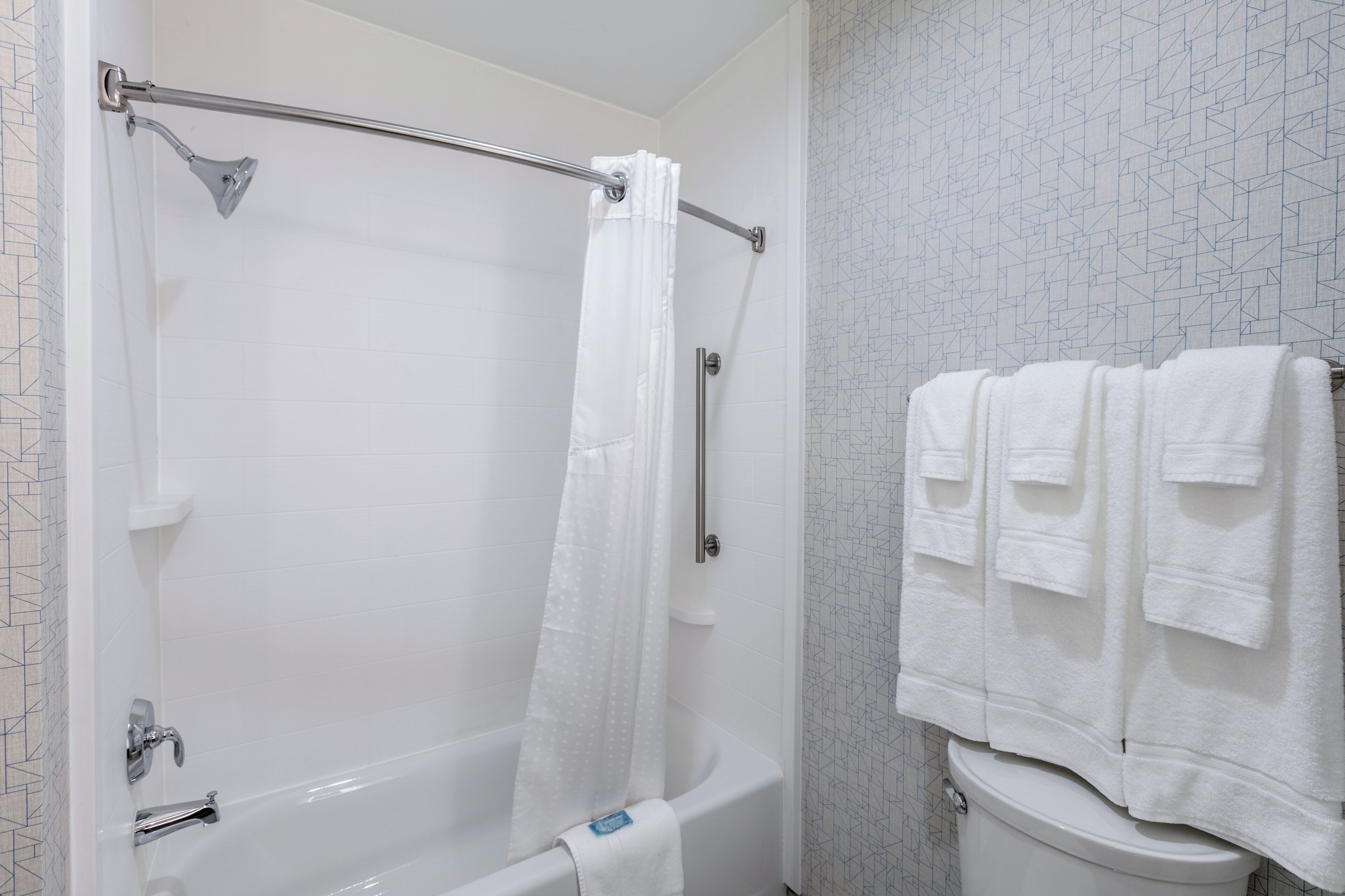 A bathroom with a bathtub, a shower curtain, a toilet, and a towel rack with towels.
