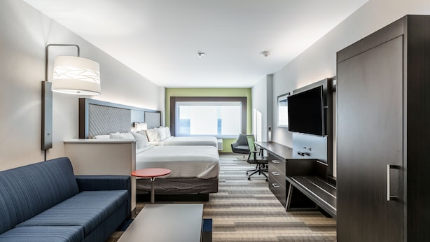 Moderni hotellihuone, jossa on sänky, sohva, työpöytä, televisio ja suuri ikkuna.