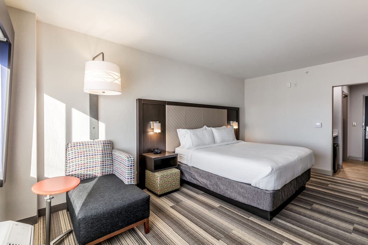 A hotel room with a bed, a desk, a chair, a nightstand, and a lamp.