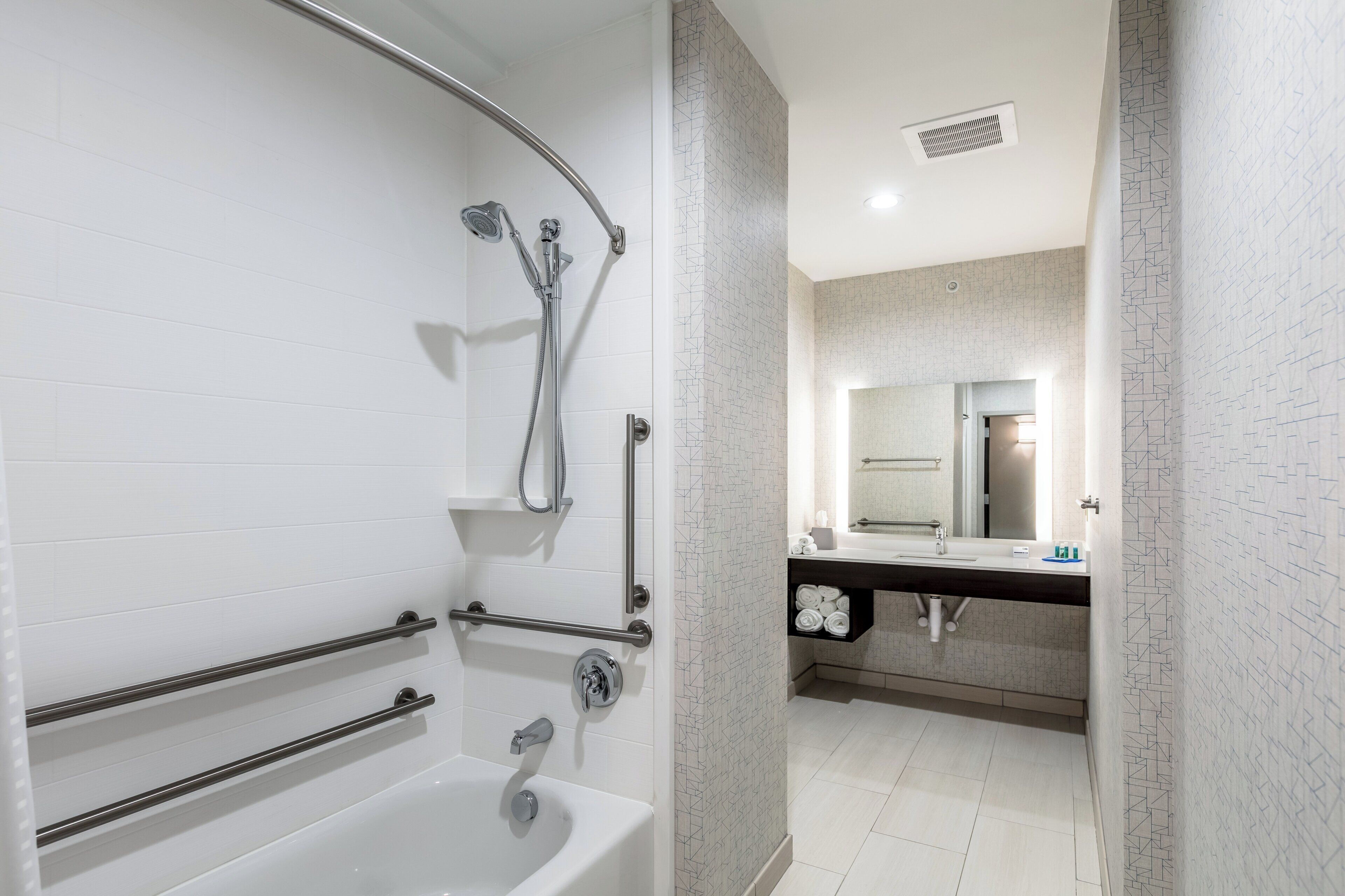 A modern bathroom with a bathtub, shower, and handrails.