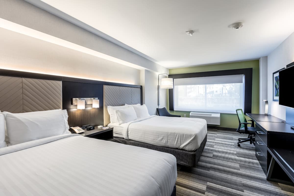 A hotel room with two beds, a desk, a chair, a TV, and a window with a view.