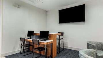 A conference room with a large flat-screen TV, a wooden table, four chairs, and a carpeted floor.