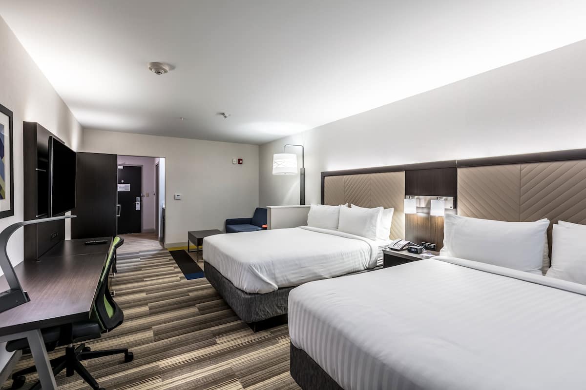 A hotel room with two beds, a desk, a chair, a lamp, and a flat-screen TV.