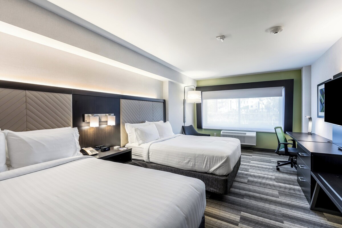 A hotel room with two beds, a desk, a chair, a TV, and a window.
