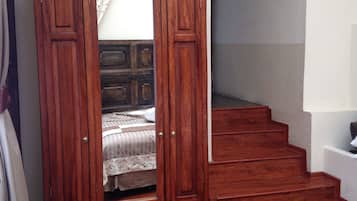 A wooden wardrobe with a mirror, a bed with a patterned bedspread, and a staircase leading to an upper level.